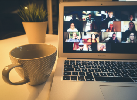 Bild mit Tasse und Laptop, auf welchem eine Zoom-Konferenz läuft